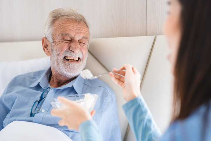 man getting fed in care home in a bed by a nurse