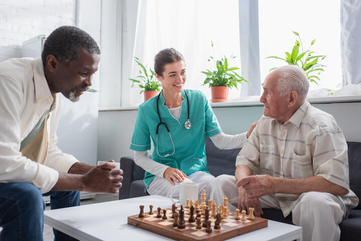 senior man playing chess with resident with nurse sitting beside him