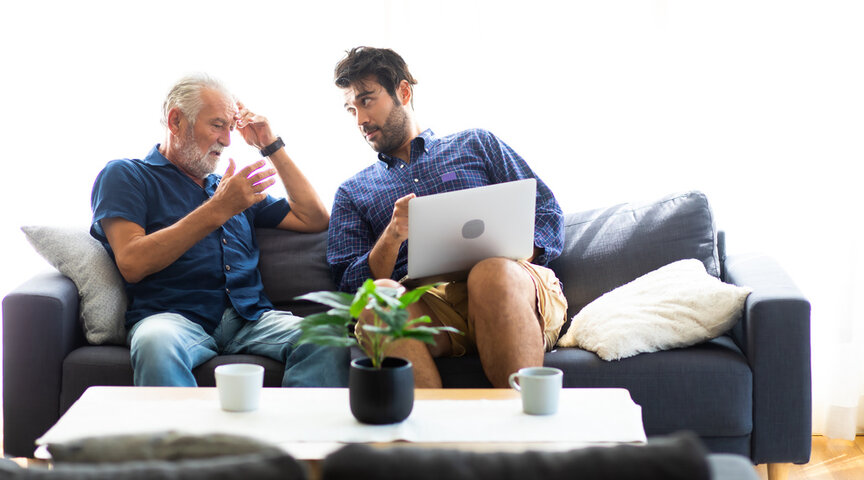 adult child having a conversation with his dad about care homes with a laptop
