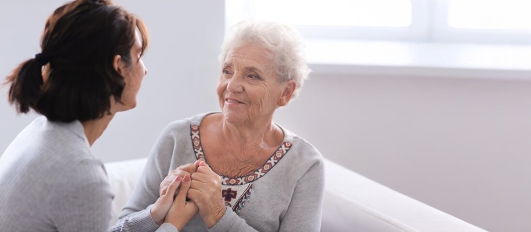 adult daughter speaking to mother on sofa smiling