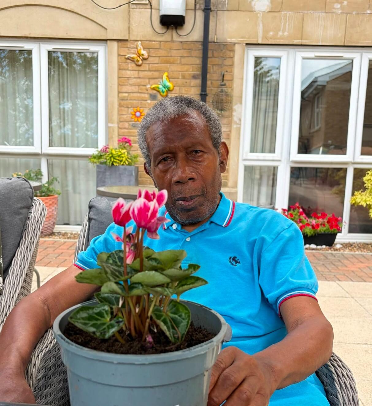 resident in a blue polo shirt holding flowers in a plant pot